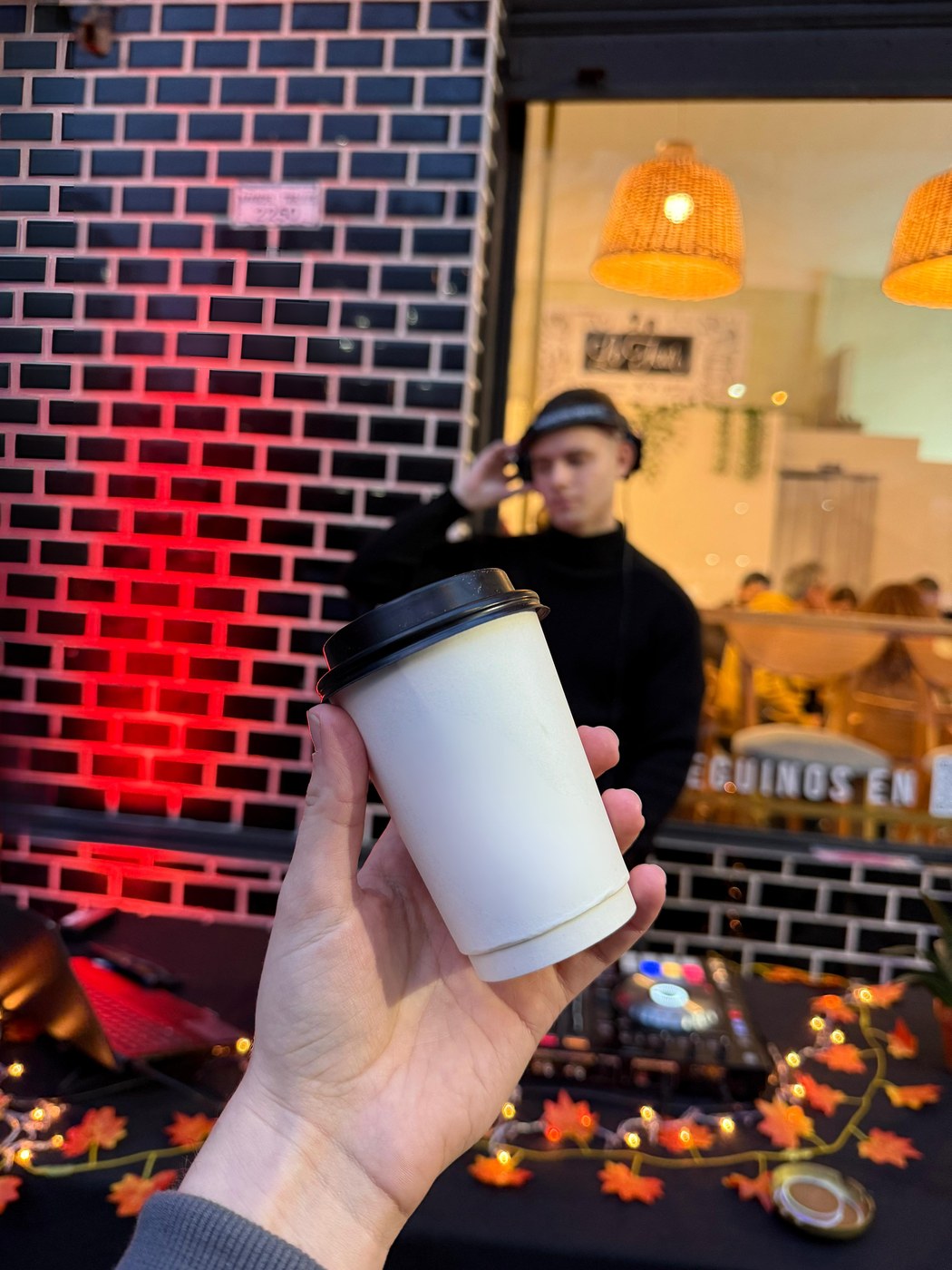 Mano sosteniendo un café de local mientras un DJ toca de fondo en una edición de Coffee & Music