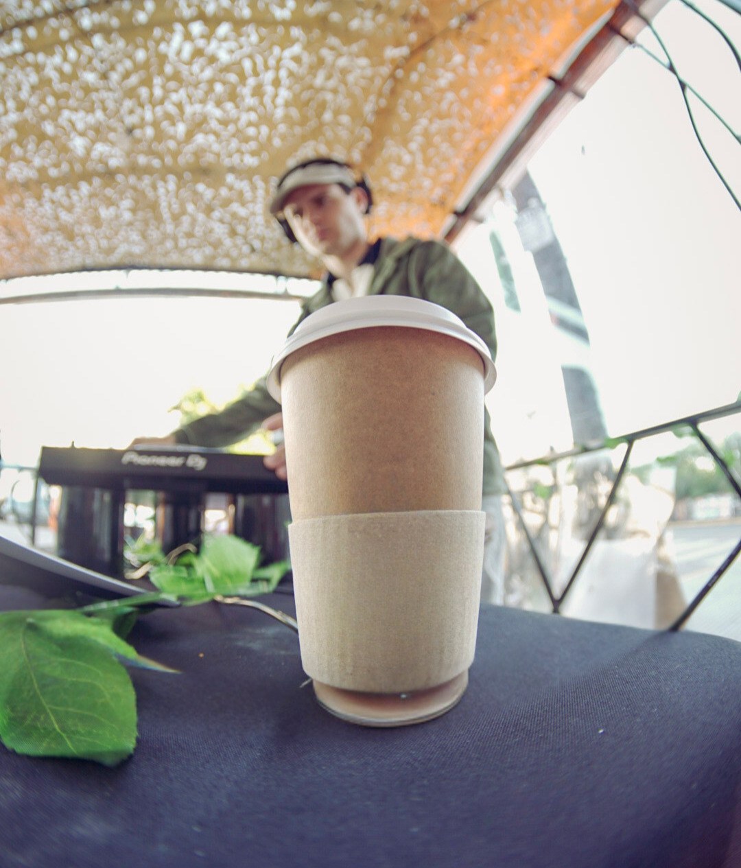Café sobre una mesa con un DJ operando una controladora Pioneer de fondo, en una terraza al aire libre