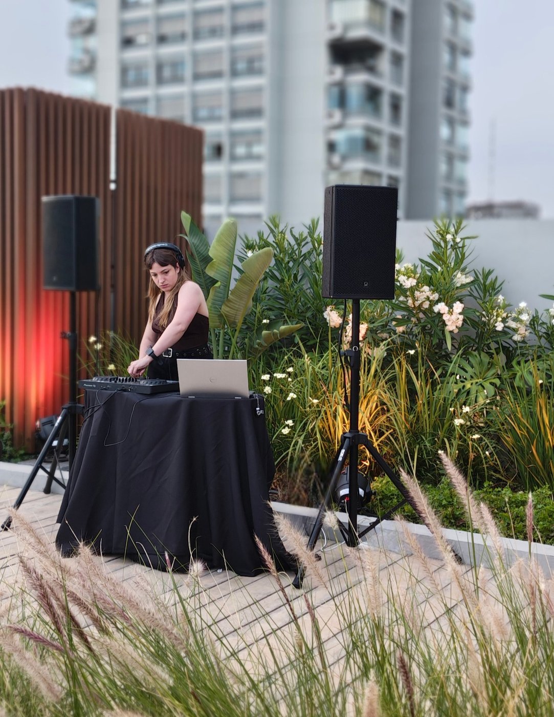 DJ operando la consola durante un evento en una terraza, de día, con edificios de fondo