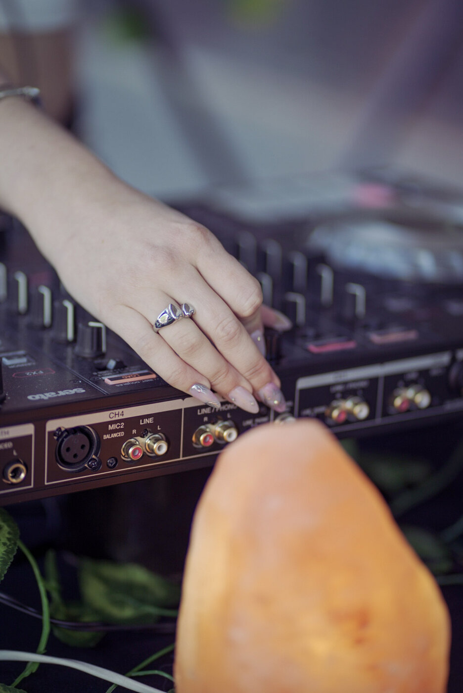 Detalle de una mano ajustando la mezcladora DJ, con una lámpara de sal en primer plano