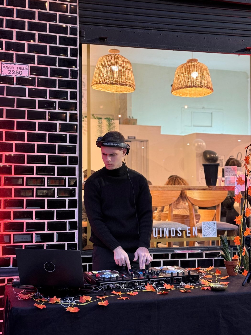DJ tocando de noche en la vidriera de un local, ambiente cálido con luces colgantes