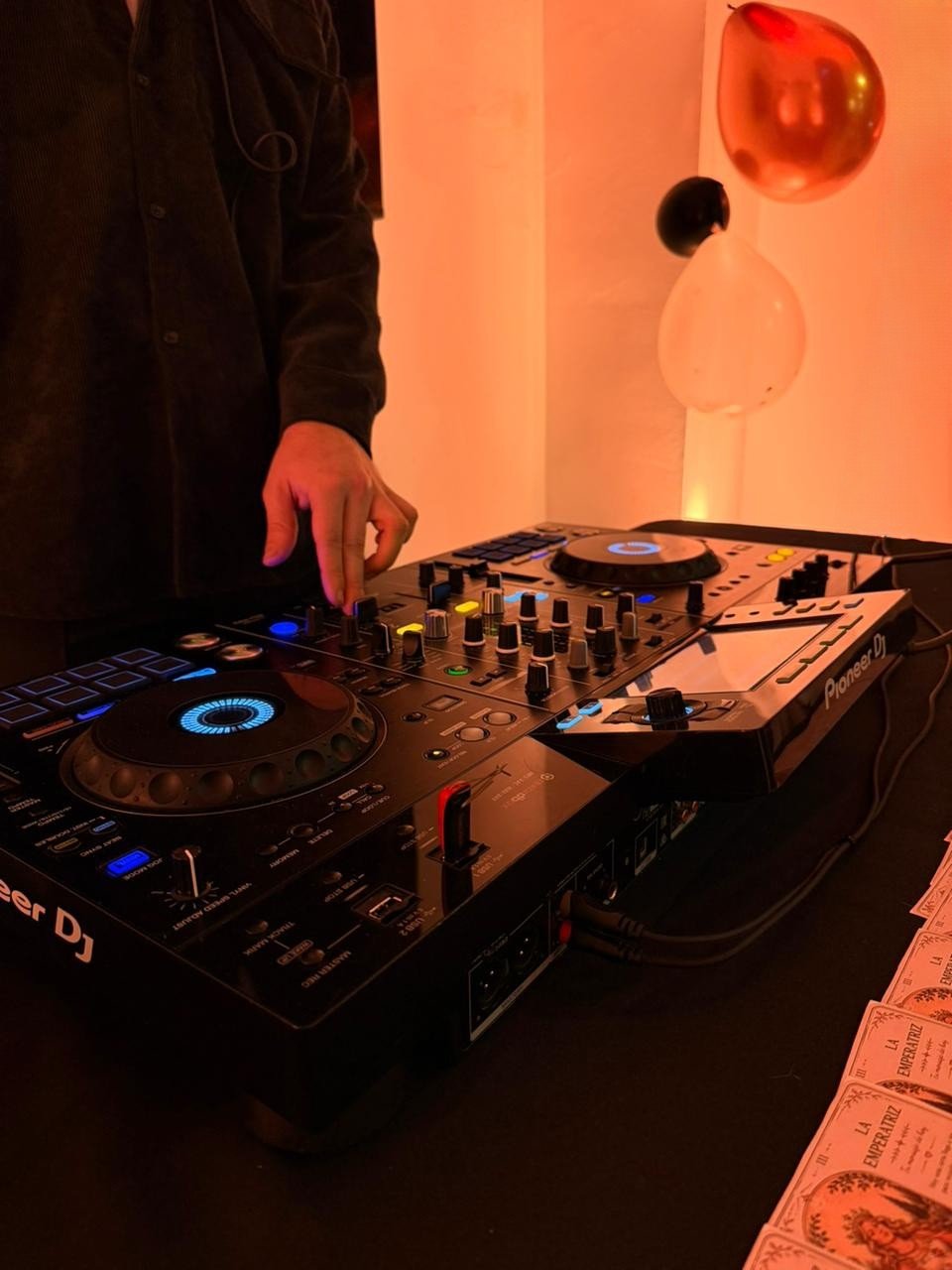 Mano ajustando la consola Pioneer DJ en un cumpleaños con iluminación cálida y globos de fondo